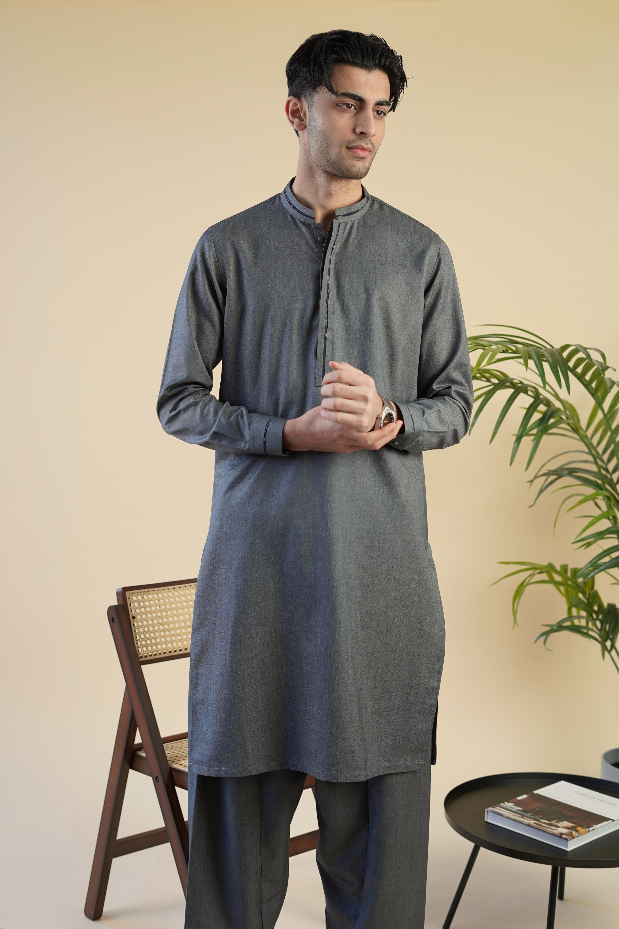 Pakistani male model wearing UD Fabrics shalwar kameez in grey with black band design on collar. Model poses with watch.