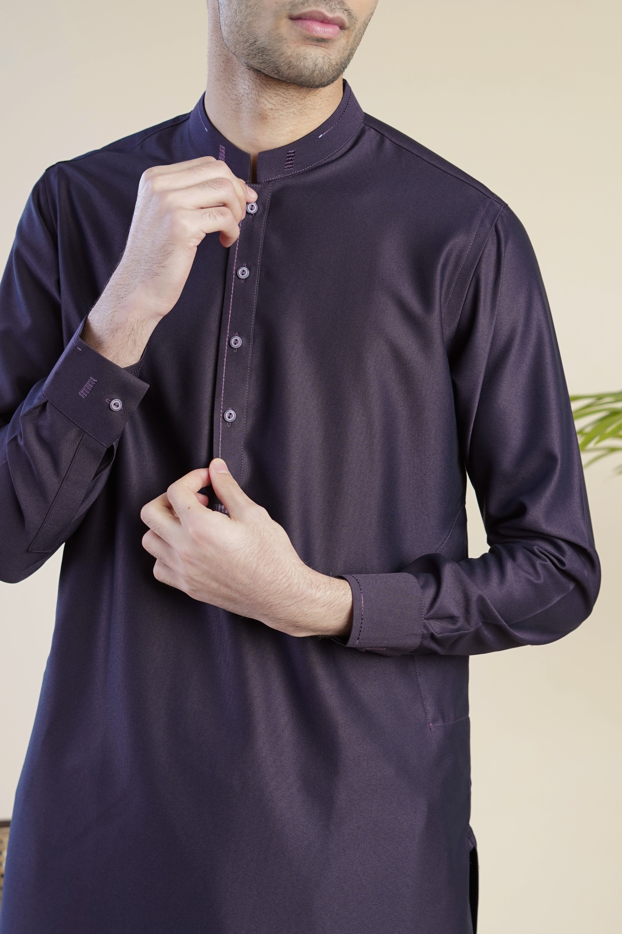 Close up, detail image of Pakistani male model standing wearing UD Fabrics men's purple shalwar kameez. Shalwar kameez with design on collar. Model poses looking away from camera