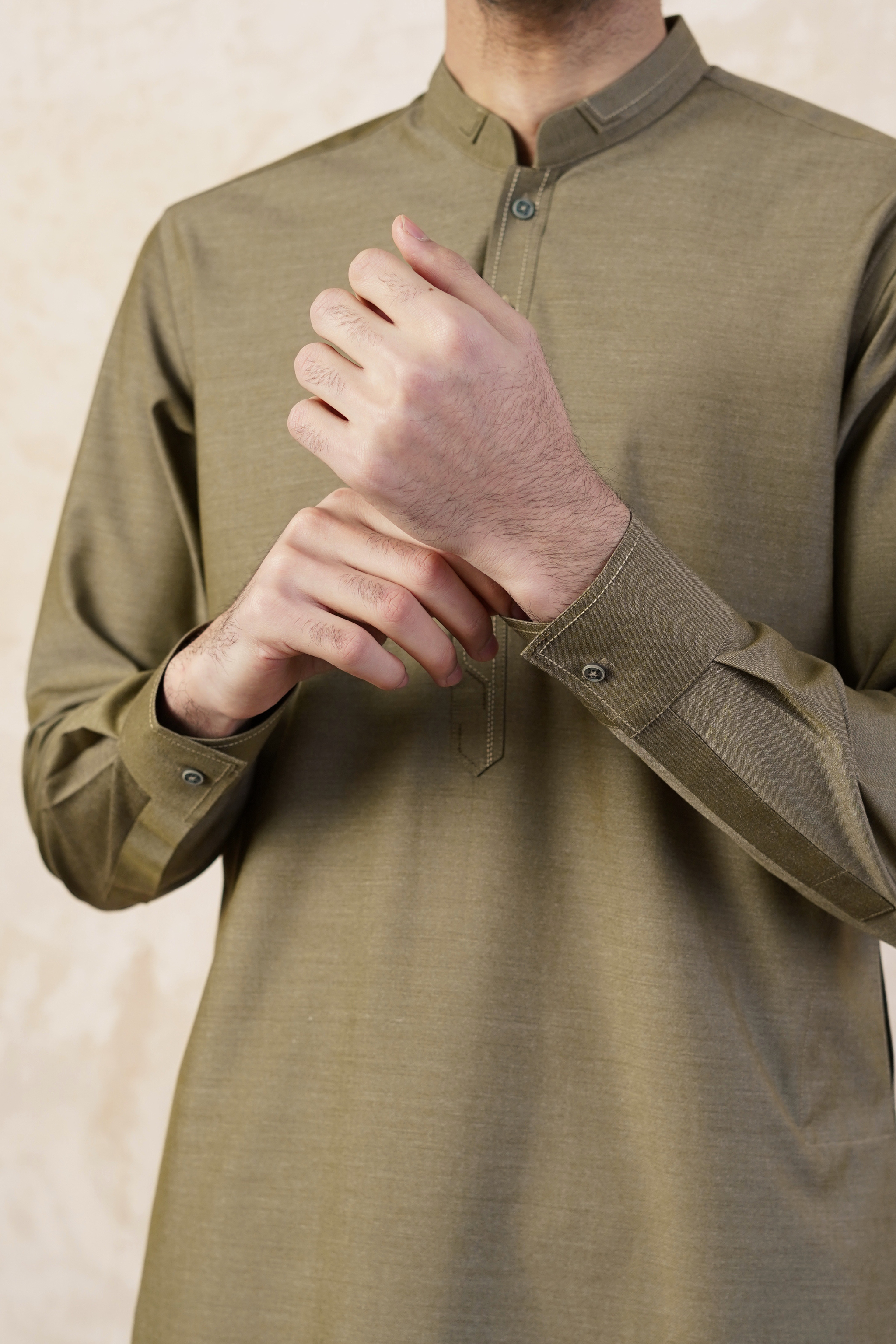 Close up, detail image of Pakistani male model standing wearing UD Fabrics men's khaki green shalwar kameez. Shalwar kameez with design on collar. Model poses looking away from camera