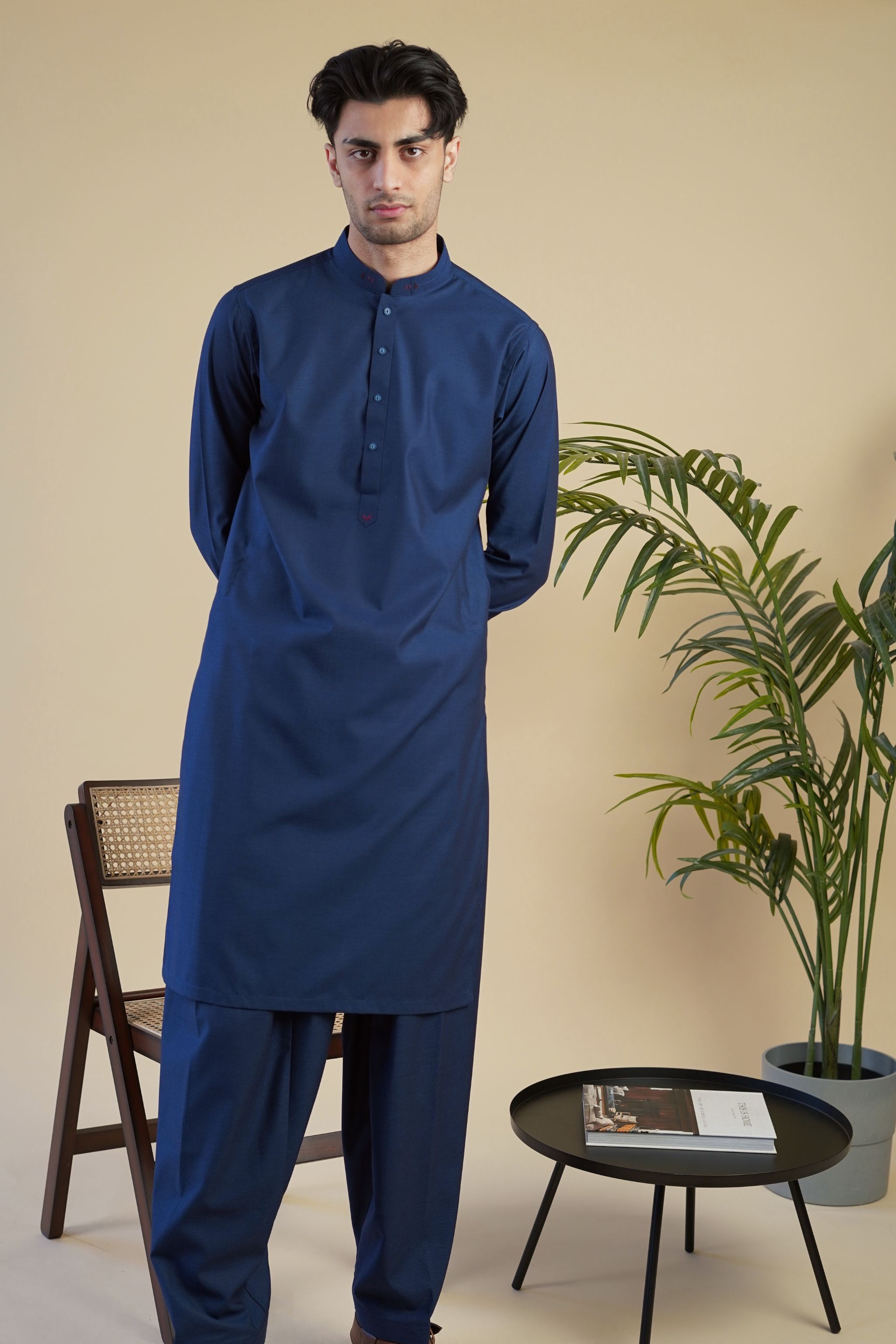 Pakistani male model standing wearing UD Fabrics men's blue shalwar kameez. Shalwar kameez with design on collar. Model poses looking towards camera