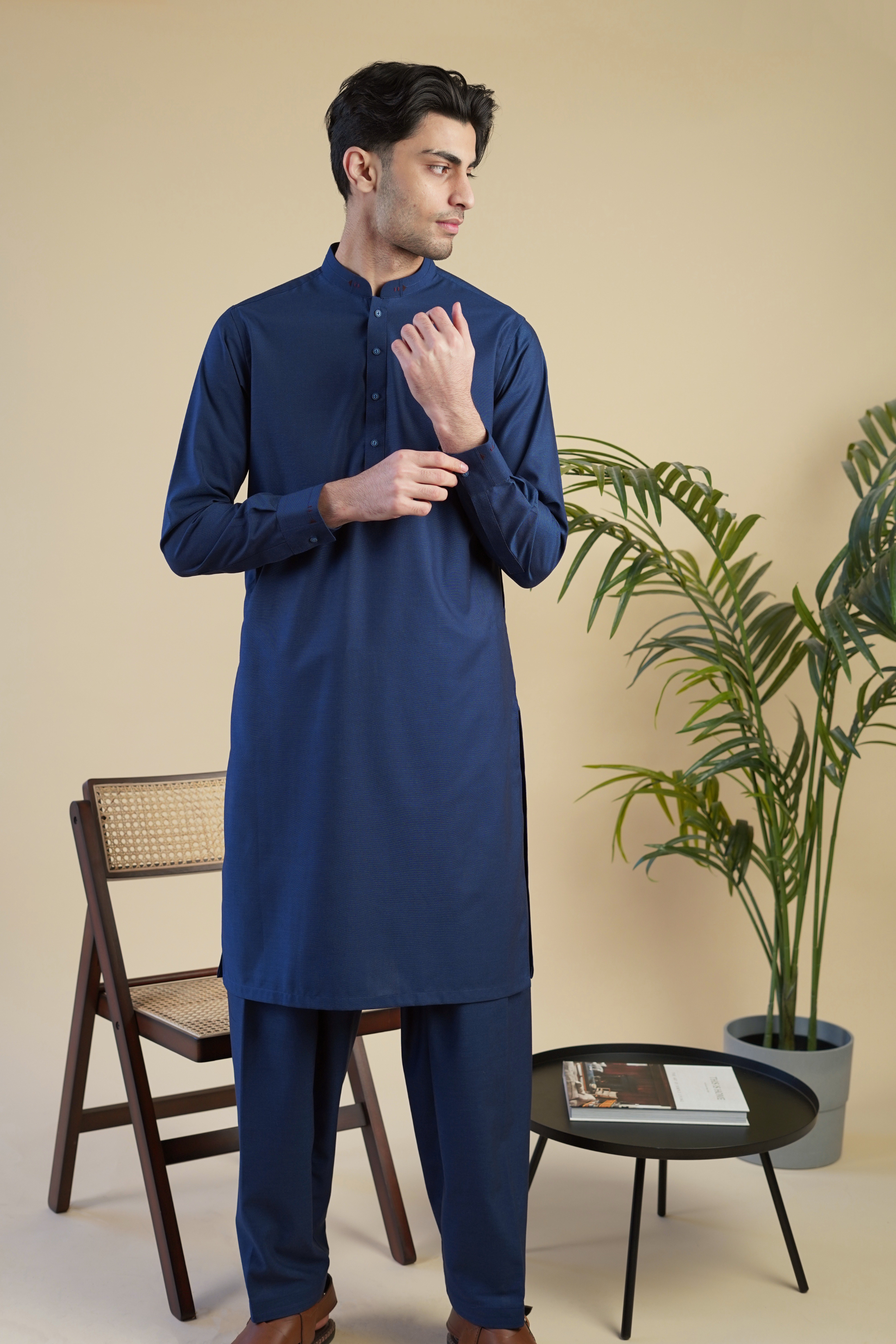 Pakistani male model standing wearing UD Fabrics men's blue shalwar kameez. Shalwar kameez with design on collar. Model poses looking away from camera. Men's pakistani clothing