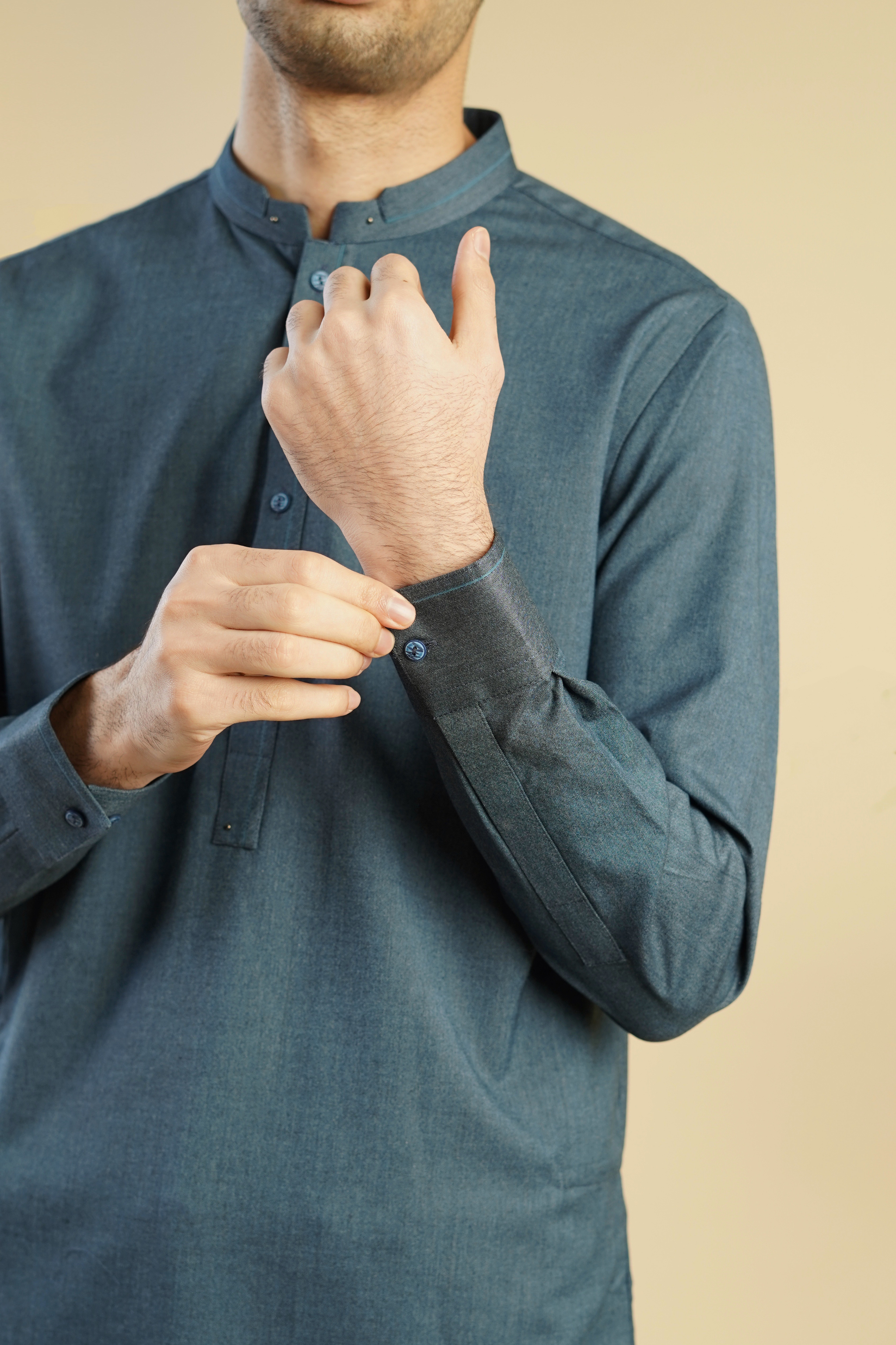 Detail close up image of Pakistani male model standing wearing UD Fabrics men's blue shalwar kameez. Shalwar kameez with design on collar. Model poses looking away from camera. Men's pakistani clothing