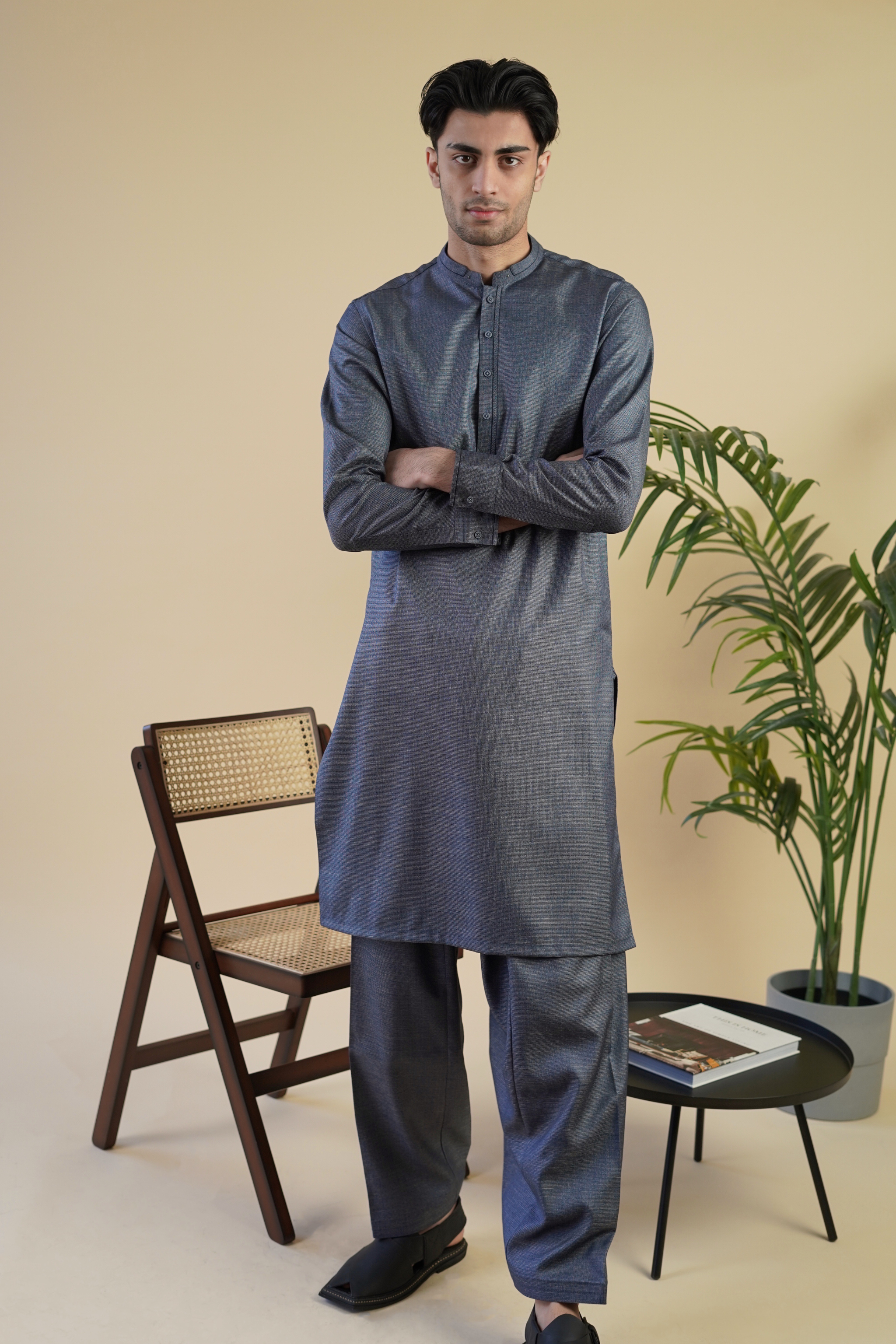 Pakistani male model standing wearing UD Fabrics men's grey shalwar kameez. Shalwar kameez with design on collar. Model poses looking toward camera. Men's pakistani clothing