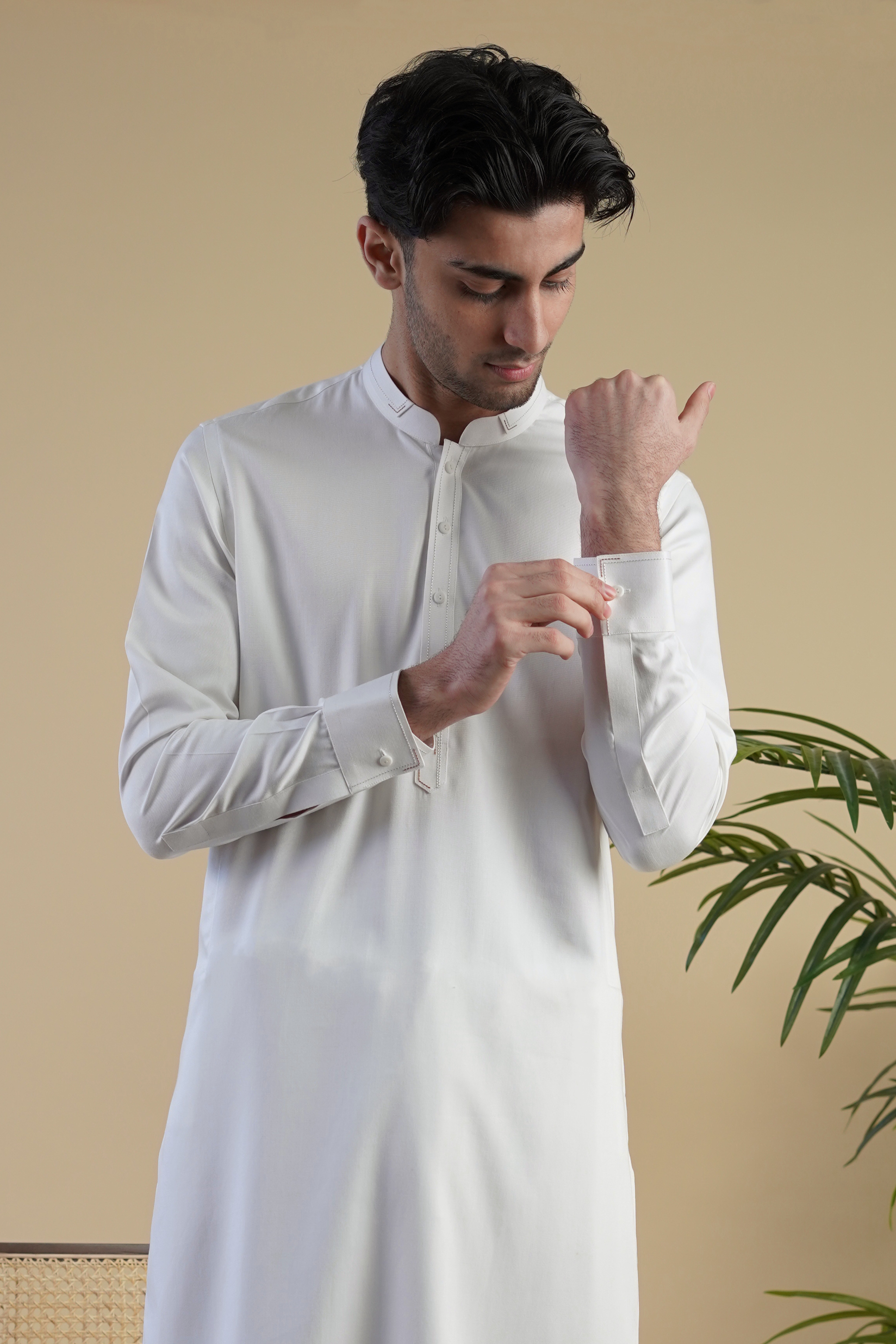 Close up detail image of Pakistani male model standing wearing UD Fabrics men's white shalwar kameez. Shalwar kameez with design on collar. Model poses looking directly toward camera. Men's pakistani clothing. White shalwar kameez