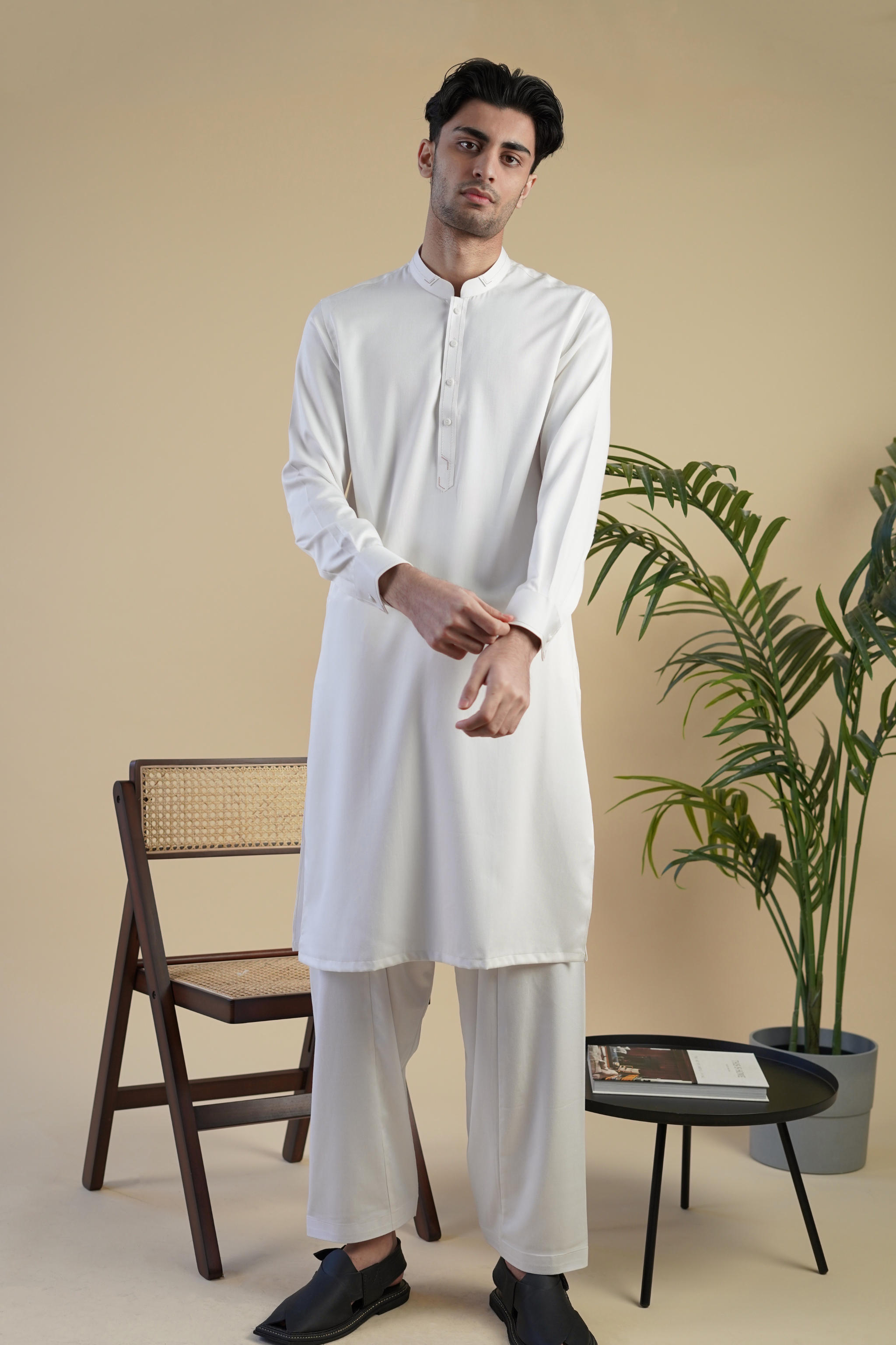 Pakistani male model standing wearing UD Fabrics men's white shalwar kameez. Shalwar kameez with design on collar. Model poses looking directly toward camera. Men's pakistani clothing. White shalwar kameez