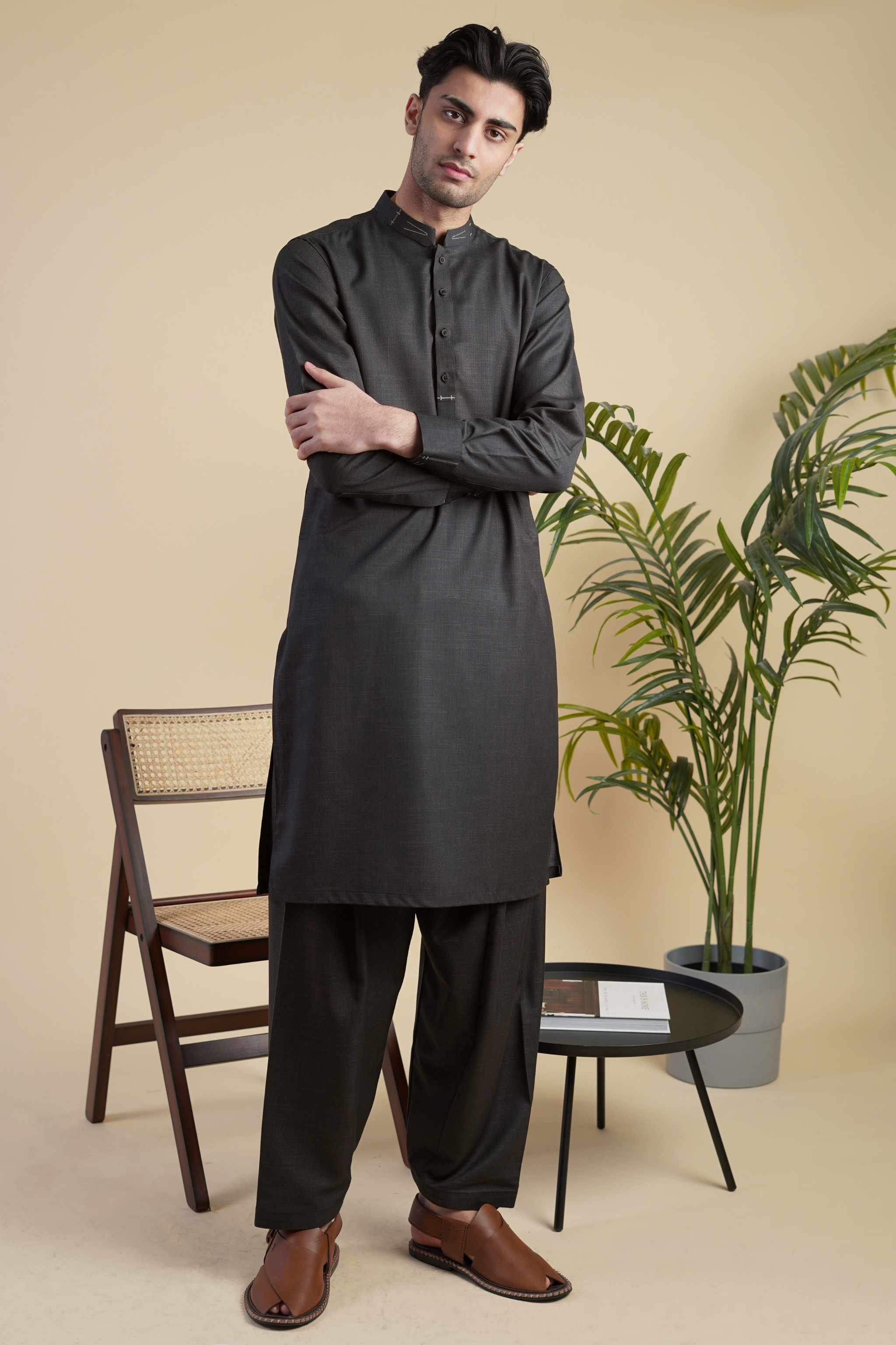 Pakistani male model standing wearing UD Fabrics men's black shalwar kameez. Shalwar kameez with design on collar. Model poses looking directly toward camera. Men's pakistani clothing. Black shalwar kameez