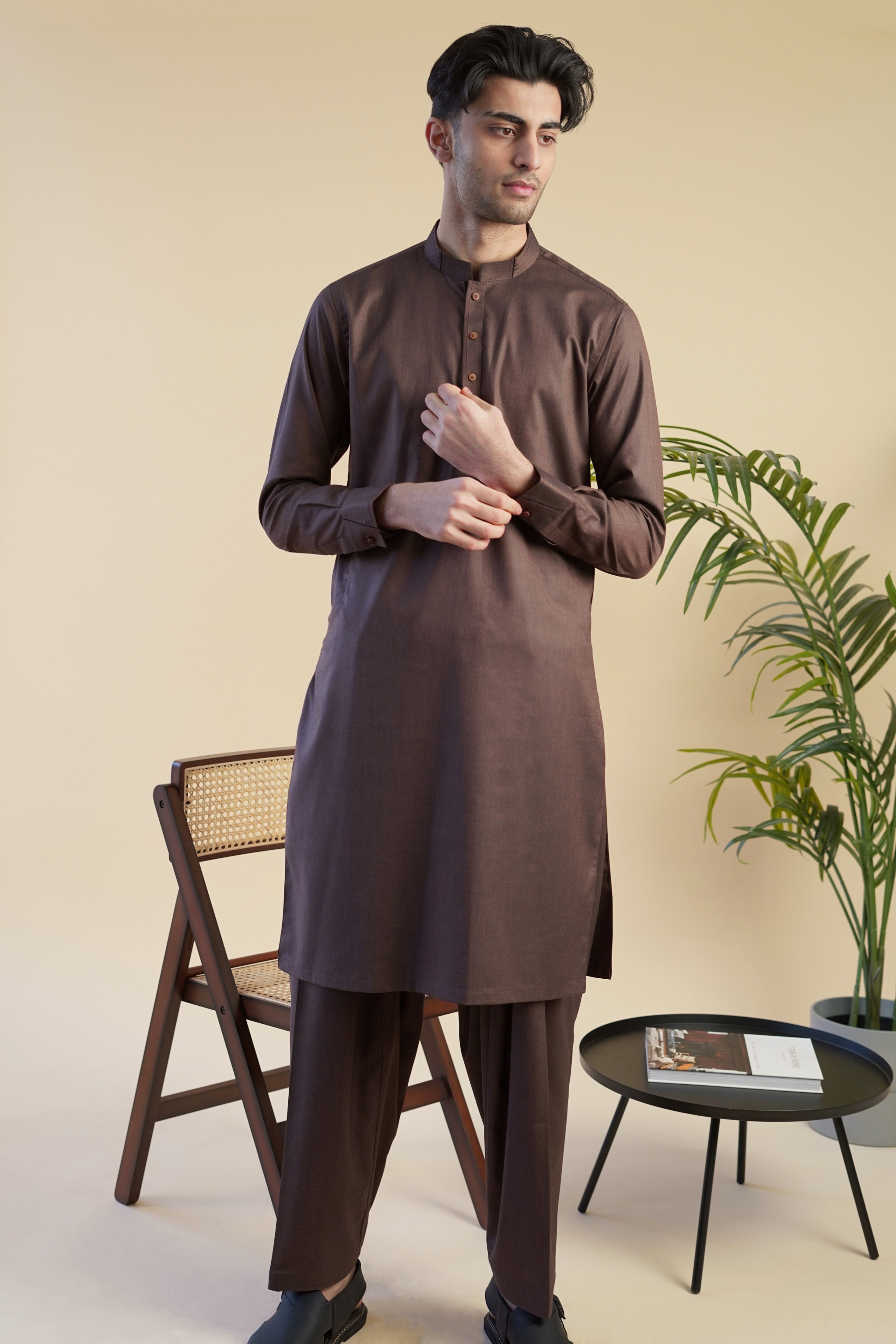 Pakistani male model wearing UD Fabrics men's brown shalwar kameez . Model poses looking away from camera