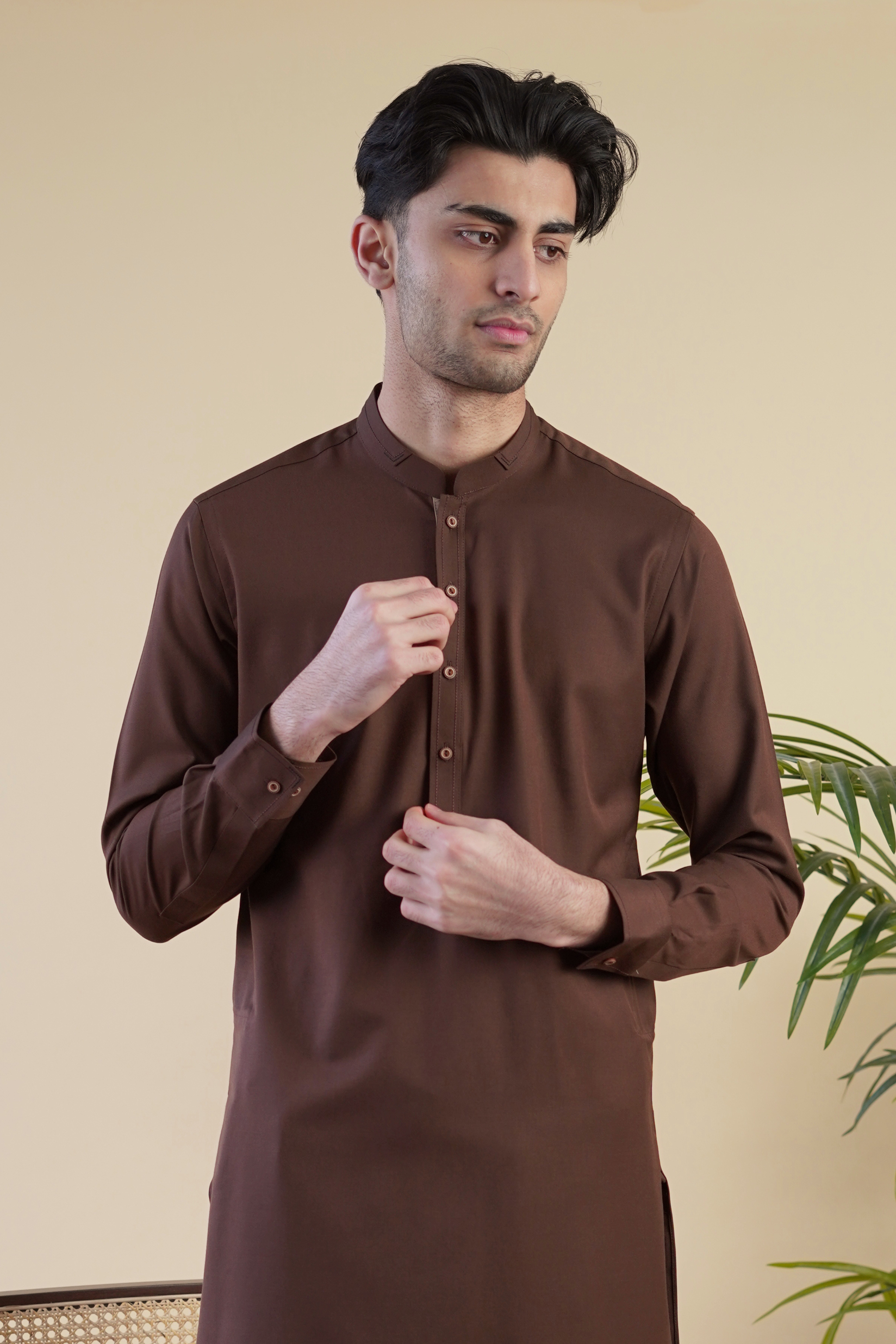 Close up, detail image of Pakistani male model wearing UD Fabrics men's brown shalwar kameez. Shalwar kameez with design on collar. Model poses looking away from camera