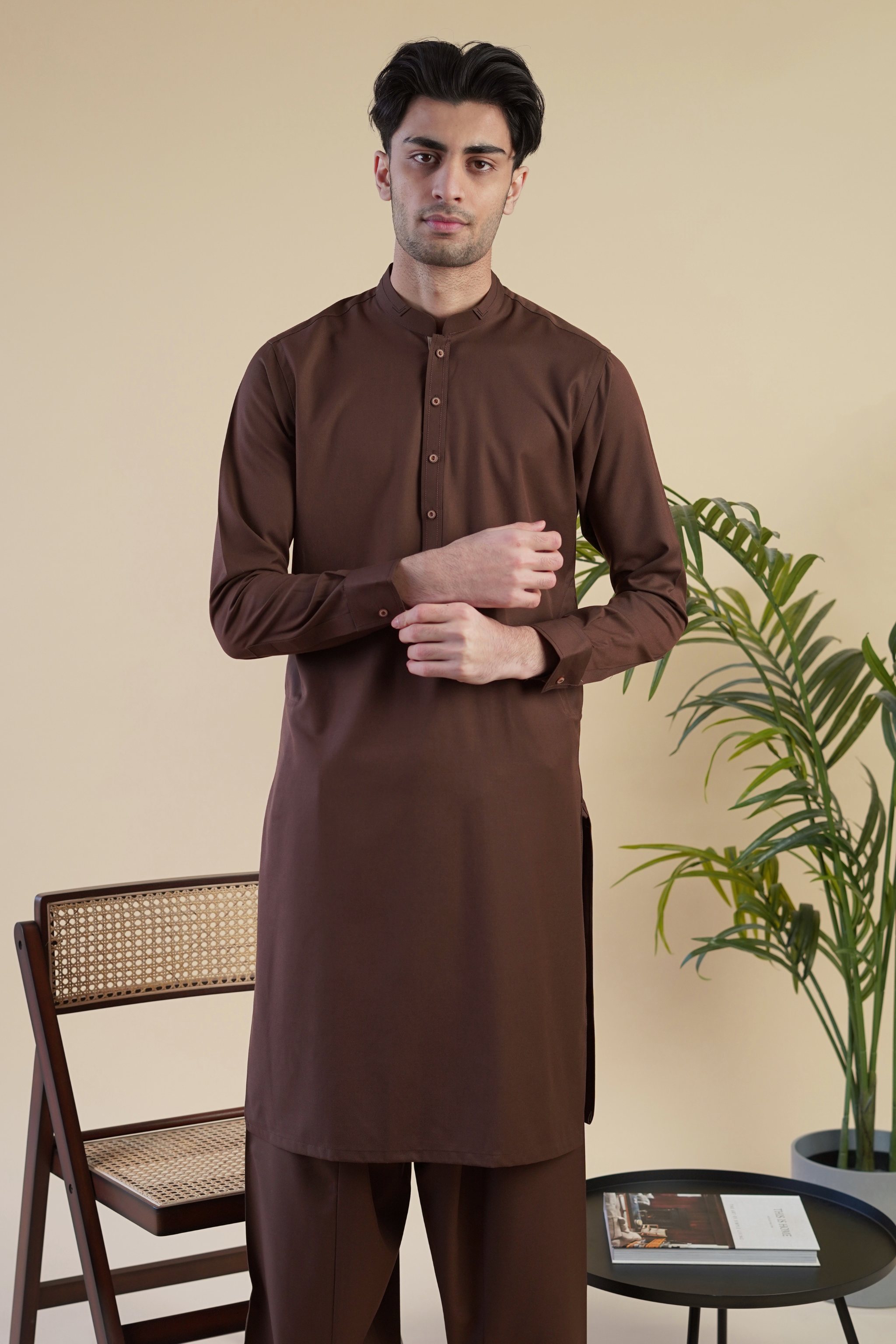 Pakistani male model wearing UD Fabrics men's brown shalwar kameez . Model poses looking toward camera.