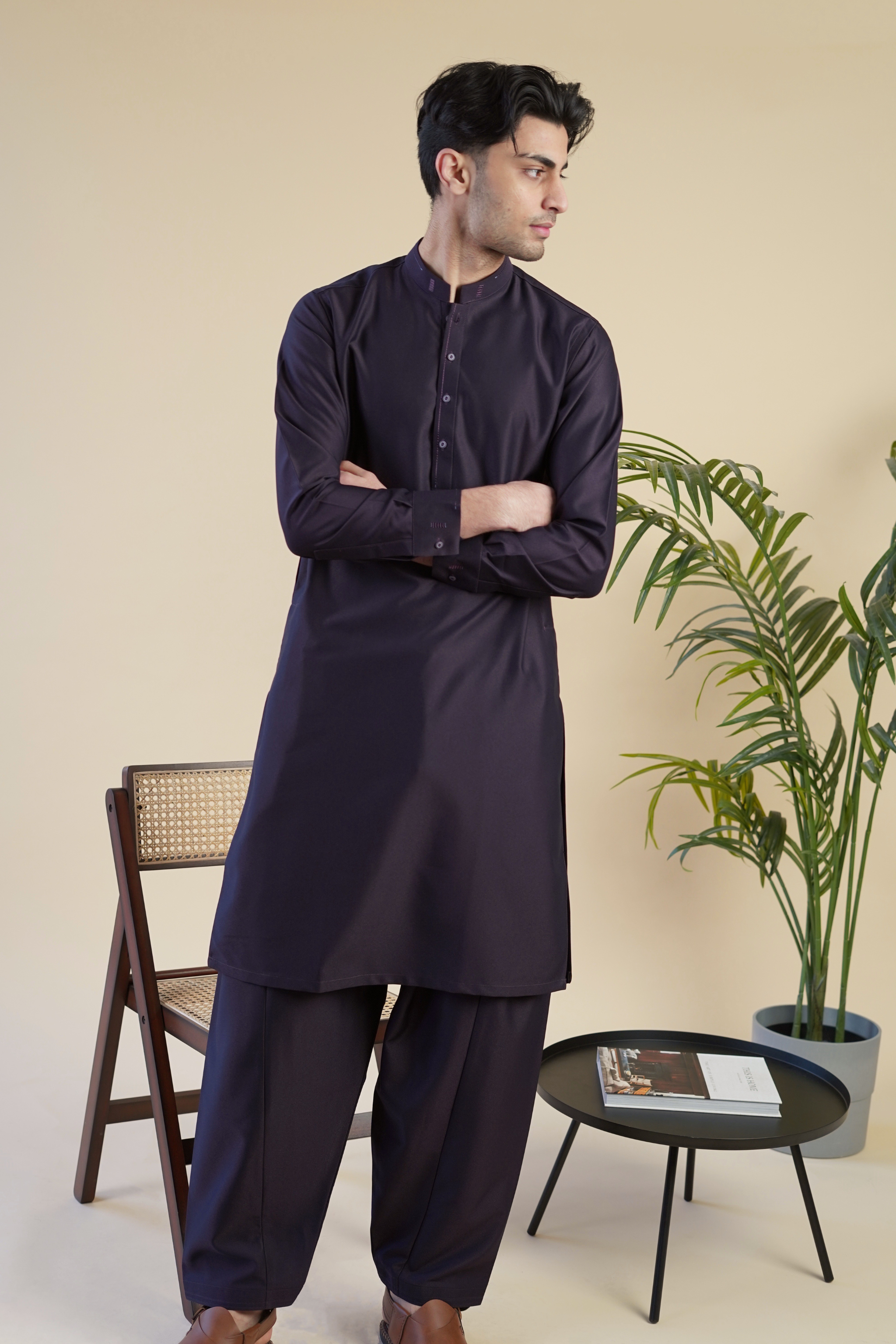 Pakistani male model standing wearing UD Fabrics men's purple shalwar kameez. Shalwar kameez with design on collar. Model poses looking away from camera